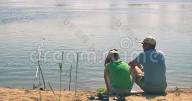 一对幸福的<strong>父子</strong>坐在河岸上，<strong>钓鱼</strong>，爸爸和儿子早上在<strong>钓鱼</strong>。 一个幸福的家庭。